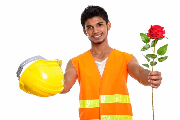 Joven trabajador de la construcción indio feliz sonriendo mientras da rosa roja