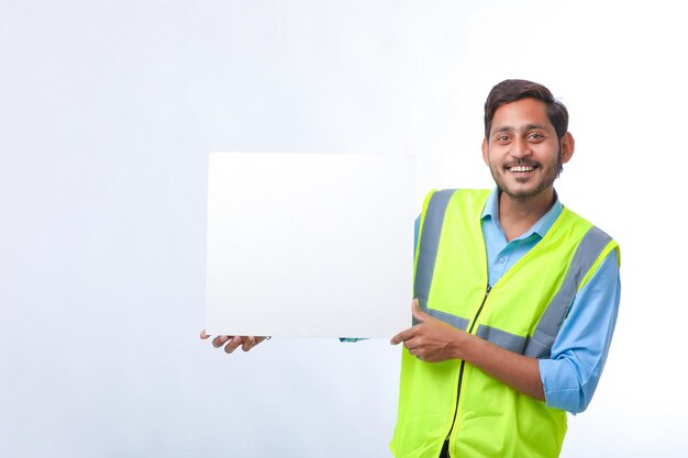 Joven trabajador de la construcción indio que muestra una cartulina vacía sobre fondo blanco.