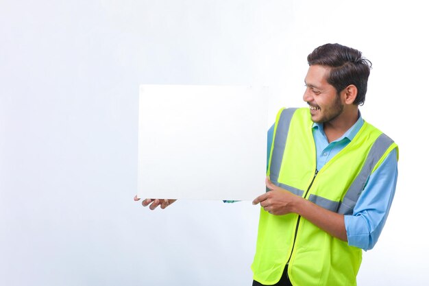 Joven trabajador de la construcción indio que muestra una cartulina vacía sobre fondo blanco.