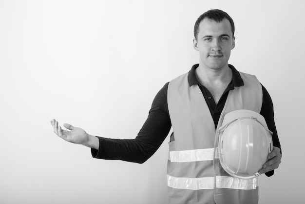 Joven trabajador de la construcción musculoso sosteniendo un casco de seguridad mientras muestra algo