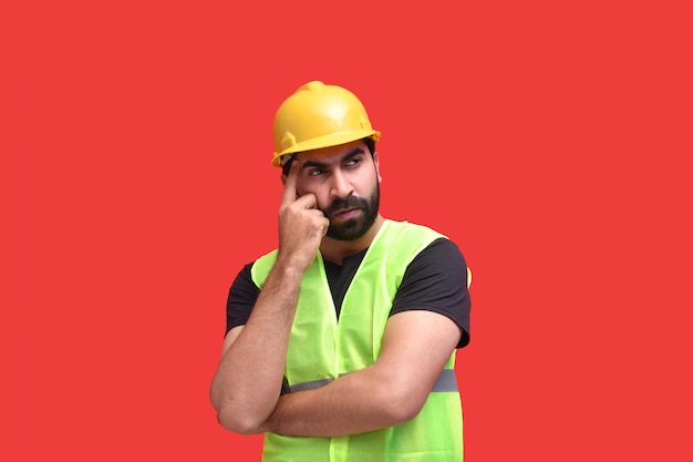 Joven trabajador de la construcción pensando sobre fondo rojo modelo paquistaní indio