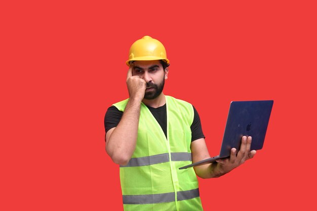 Joven trabajador de la construcción pensando y sosteniendo portátil modelo paquistaní indio