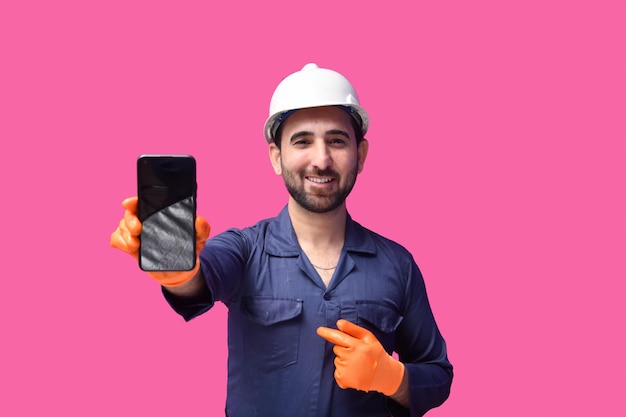 Joven trabajador de la construcción sonriendo y mostrando teléfono modelo paquistaní indio