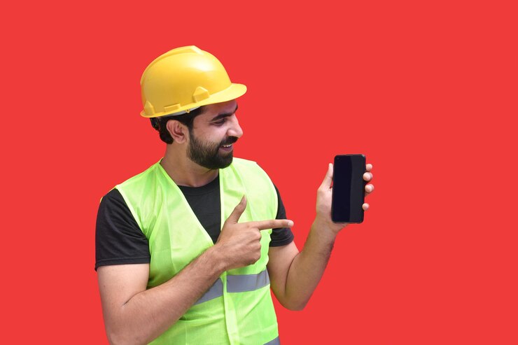 Foto joven trabajador de la construcción sonriendo sosteniendo el teléfono y mirándolo modelo paquistaní indio