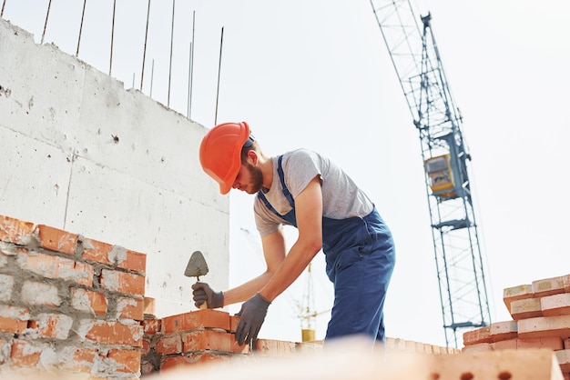 El joven trabajador de la construcción uniformado está ocupado en el edificio sin terminar