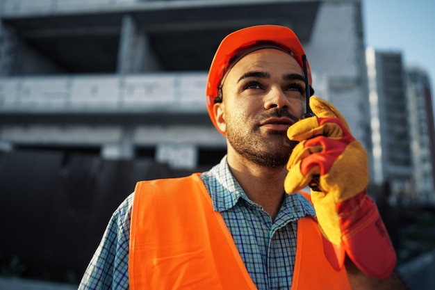 Joven trabajador de la construcción en uniforme con walkie talkie en el sitio