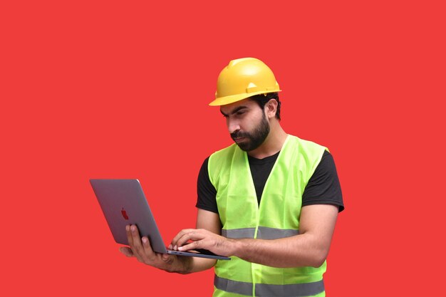 Joven trabajador de la construcción vistiendo chaqueta de seguridad con halmet y usando laptop modelo paquistaní indio