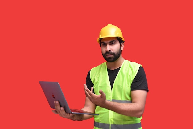 Joven trabajador de la construcción vistiendo chaqueta de seguridad con halmet y usando laptop modelo paquistaní indio