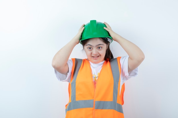 Joven trabajador de la construcción vistiendo su casco verde sobre pared blanca