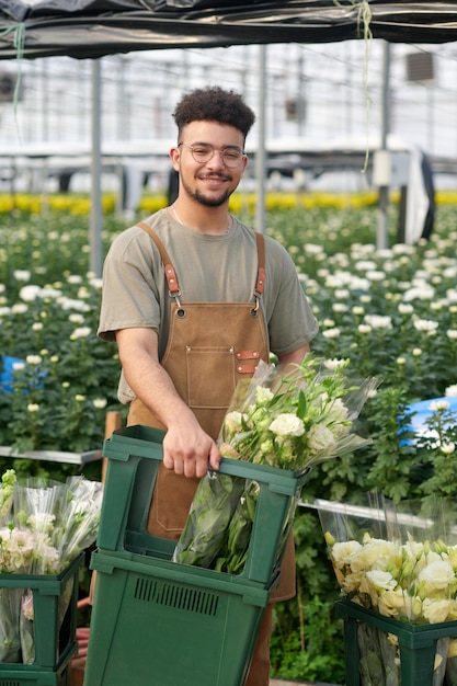 Joven trabajador feliz de un invernadero industrial con ramos de flores frescas