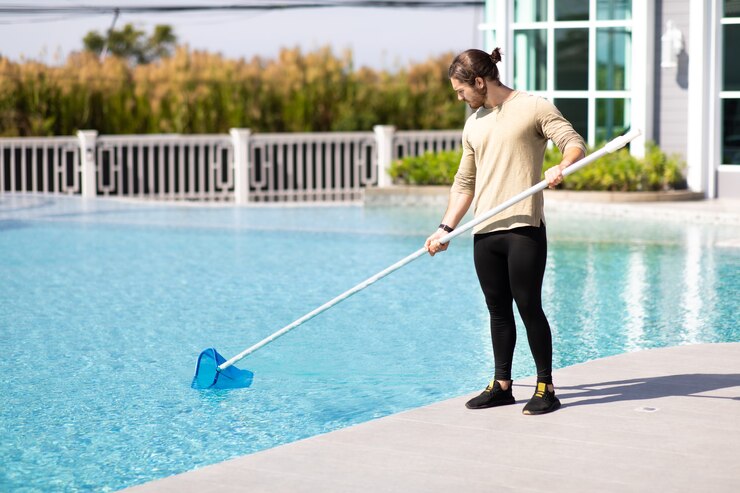 Joven trabajador limpiador profesional limpieza piscina con red de pala al aire libre.