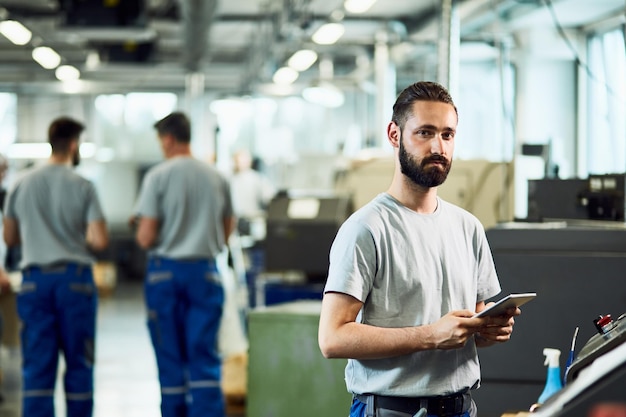 Joven trabajador manual que usa una tableta digital mientras opera una máquina CNC en una fábrica