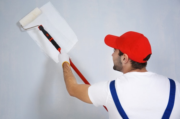 Joven trabajador pintando la pared en la habitación