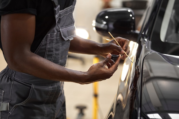 Joven trabajador de servicio de automóviles afro está pintando detalles del coche