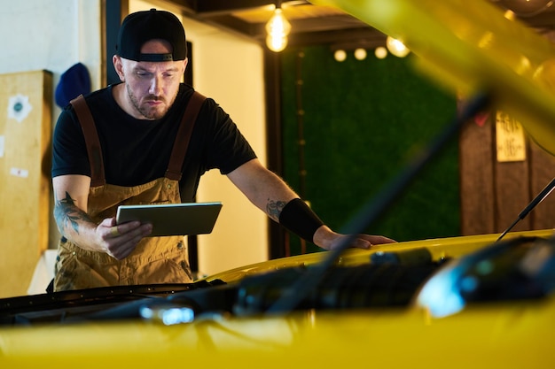 Joven trabajador del servicio de mantenimiento mirando la pantalla de la tableta durante el trabajo