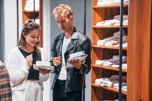 Joven trabajadora ayudando a un chico a elegir ropa en una tienda moderna con ropa cara para hombres