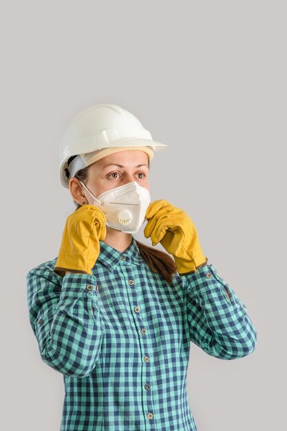 Una joven trabajadora de la construcción se pone una máscara médica protectora. Una ingeniera con un casco que lleva un respirador N95 y guantes amarillos.