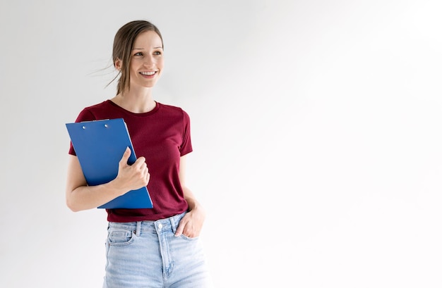 Foto joven trabajadora informal de la empresa sosteniendo una carpeta de archivos de pie sobre fondo blanco.