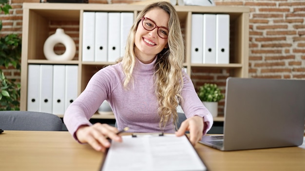 Joven trabajadora de negocios rubia que ofrece un documento para firmar en la oficina