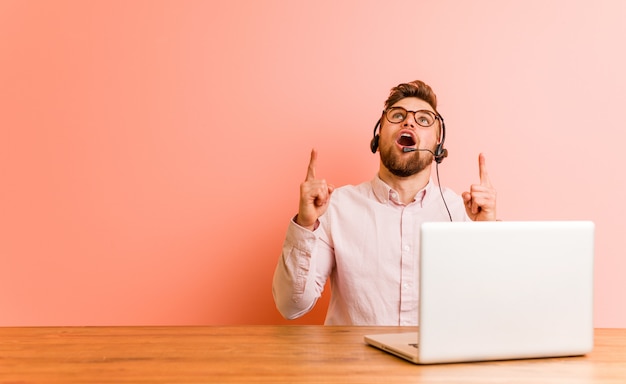 Joven trabajando en un call center apuntando al revés con la boca abierta.