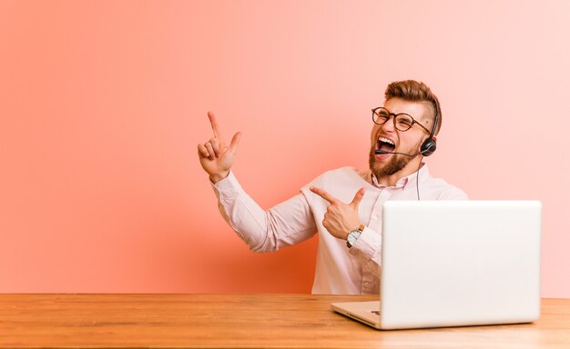 Joven trabajando en un call center apuntando con los dedos a un espacio de copia, expresando emoción y deseo.