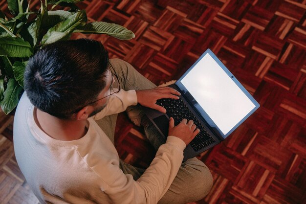 Joven trabajando en casa con una laptop sentada en el suelo rodeada de plantas de interior