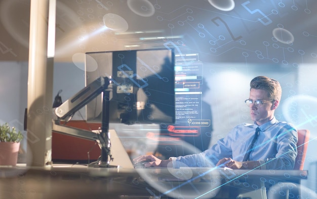 Joven trabajando en una computadora por la noche en una oficina oscura. El diseñador trabaja en la época posterior.