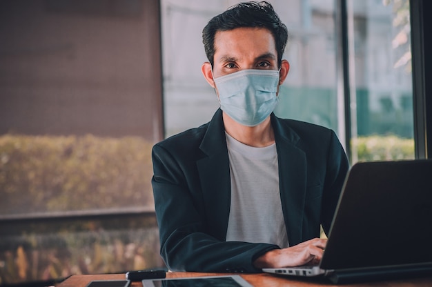 Joven trabajando en una computadora portátil con una máscara protectora