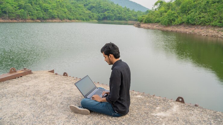 Joven trabajando en una computadora portátil y sentado en la naturaleza Concepto de trabajo y nómada digital