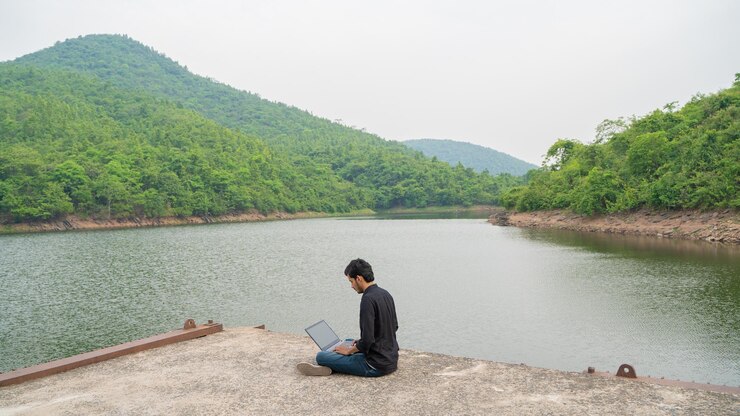 Joven trabajando en una computadora portátil y sentado en la naturaleza Concepto de trabajo y nómada digital