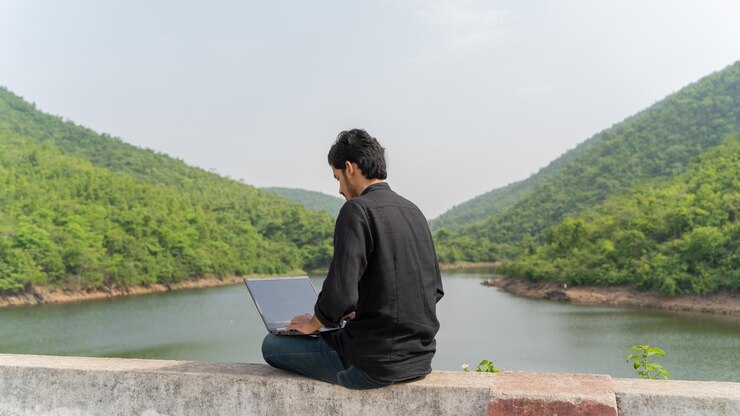 Joven trabajando en una computadora portátil y sentado en la naturaleza Concepto de trabajo y nómada digital