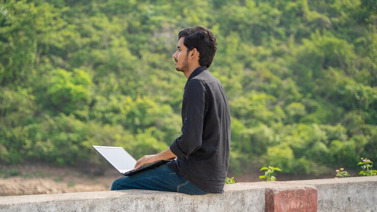 Joven trabajando en una computadora portátil y sentado en la naturaleza Concepto de trabajo y nómada digital