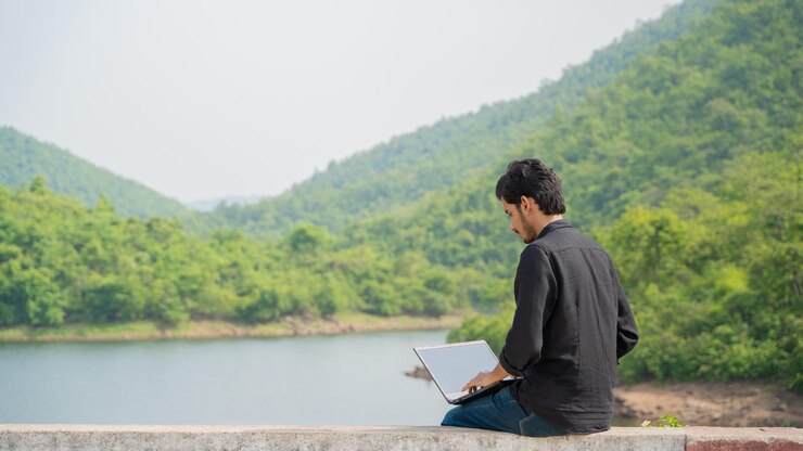 Joven trabajando en una computadora portátil y sentado en la naturaleza Concepto de trabajo y nómada digital