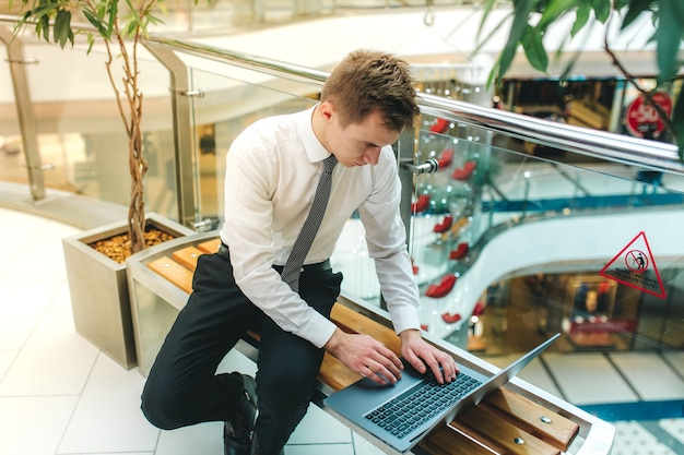 Joven trabajando en un cuaderno, con camisa blanca, sentado en una silla, estudiante serio, aprendiendo en la computadora