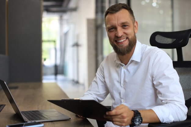 Foto joven está trabajando con papeles mientras está sentado en la oficina. el empresario exitoso está estudiando documentos con mirada atenta y concentrada.