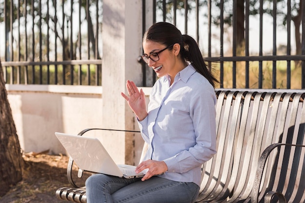 Joven trabajando en su computadora al aire libre en una tarde soleada sentada en un banco en el parque