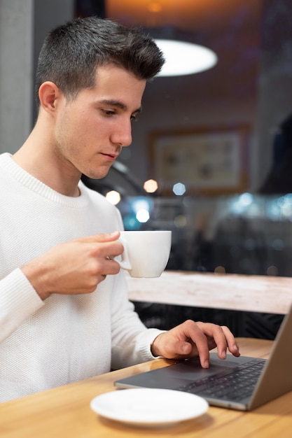 Joven trabajando en su computadora portátil en una cafetería, joven estudiante escribiendo en la computadora.