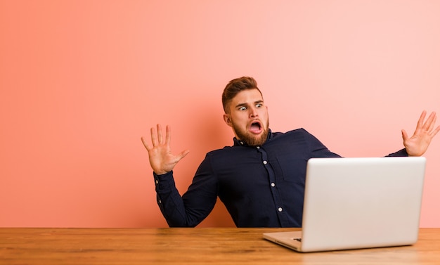 Joven trabajando con su computadora portátil en estado de shock debido a un peligro inminente