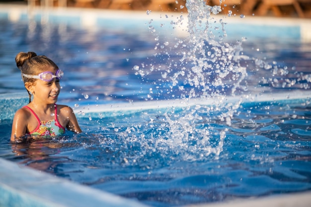 Una joven con un traje de baño de leopardo brillante nada con una pelota inflable de colores brillantes en una piscina azul profunda con agua transparente en una cálida tarde soleada de verano