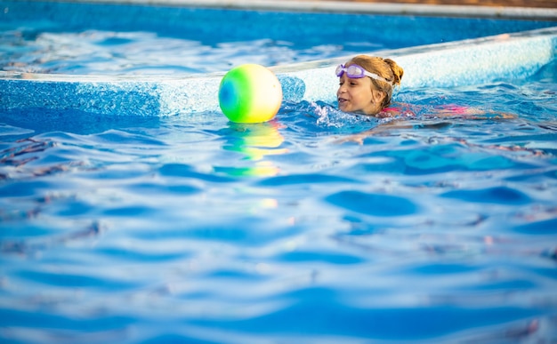 Una joven con un traje de baño de leopardo brillante nada con una pelota inflable de colores brillantes en una piscina azul profunda con agua transparente en una cálida tarde soleada de verano