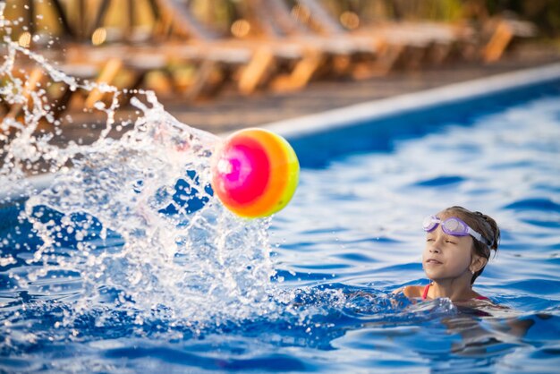 Una joven con un traje de baño de leopardo brillante nada con una pelota inflable de colores brillantes en una piscina azul profunda con agua transparente en una cálida tarde soleada de verano