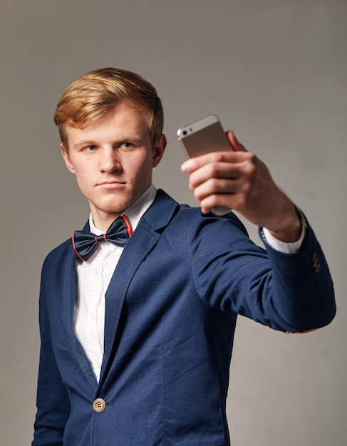 Joven de traje con corbata de moño tomando selfie con celular.