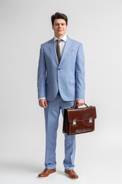 Joven con traje de negocios azul, camisa blanca y corbata con un maletín de cuero