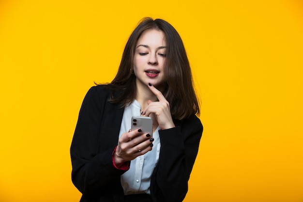 Una joven con traje de negocios está escribiendo en su teléfono con un fondo amarillo