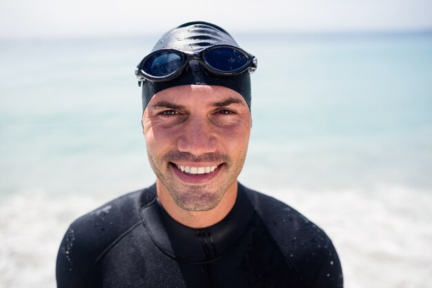 Joven en traje de neopreno y gafas de natación de pie en la playa