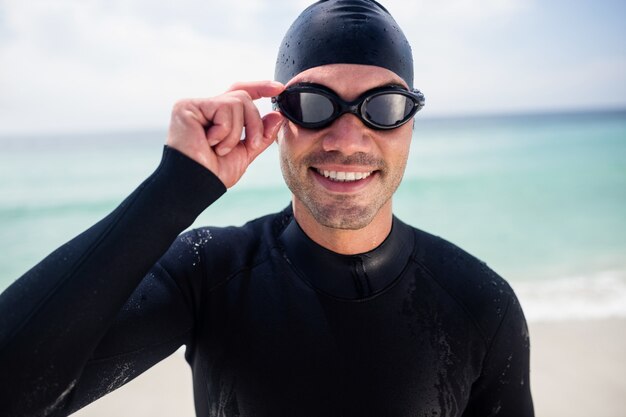 Joven en traje de neopreno y gafas de natación de pie en la playa