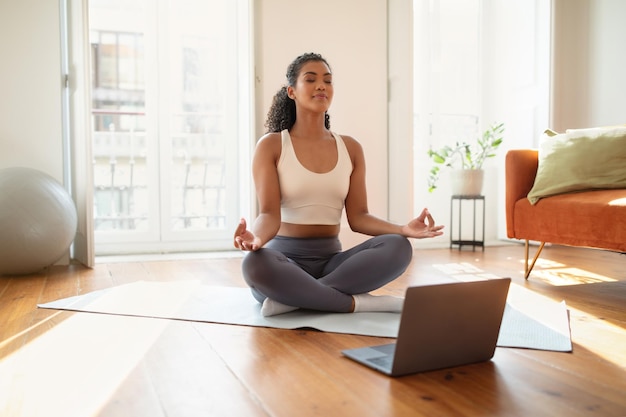 Una joven tranquila practica la meditación de atención plena en su computadora portátil en casa