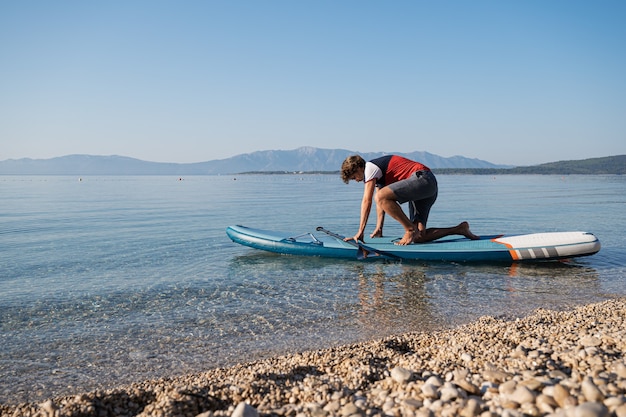 Joven tratando de ponerse de pie en un tablero de sup en el mar de la hermosa mañana en calma por Pebble Beach.