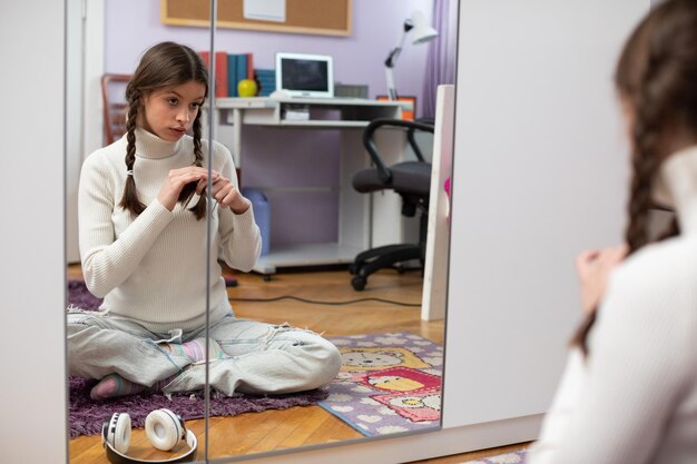 Foto una joven se trenza el cabello mientras está sentada con las piernas cruzadas frente a un espejo