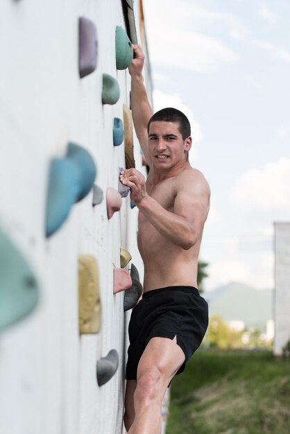 Joven trepa por una pared de roca al aire libre y claramente está decidido a llegar a la cima